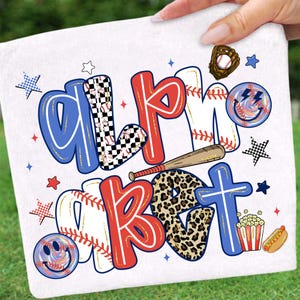 Op de afbeelding: Witte handdoek met de woorden "ALPHABET" en "BASEBALL" in rood, blauw en zwart. De letters zijn versierd met honkballen, luipaardprint en dambordpatronen. Inclusief honkbalhandschoen, knuppel en smiley gezichten.