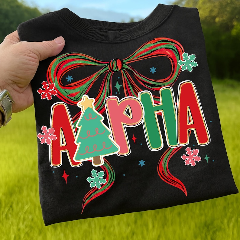 May include: Black sweatshirt with a festive design. The word "ALPHA" is displayed in red, pink, and green, with a Christmas tree graphic. A large red and green bow and snowflakes complete the holiday theme.