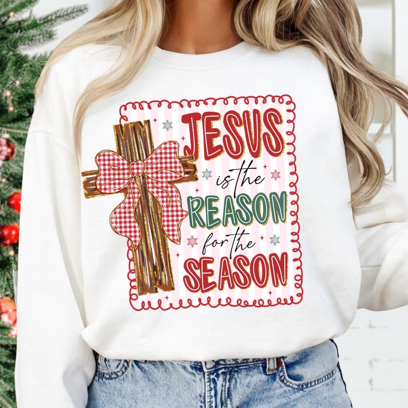 May include: White sweatshirt with a Christmas-themed graphic. The design features a wooden cross with a red and white plaid bow, and the text "JESUS is the REASON for the SEASON" in red and green.