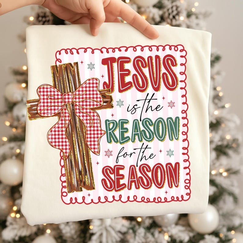 May include: Cream-colored t-shirt featuring a decorative cross with a red and white plaid bow. The shirt has the text "JESUS is the REASON for the SEASON" in red, green, and blue, with snowflake accents, perfect for Christmas.