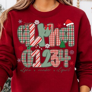 May include: A red sweatshirt with a festive design. The design includes the word "alpha" and numbers 0, 1, 2, 3, and 4, along with snowflakes, a Christmas tree, and a Santa hat. The text "alpha + number + clipart" is also included.