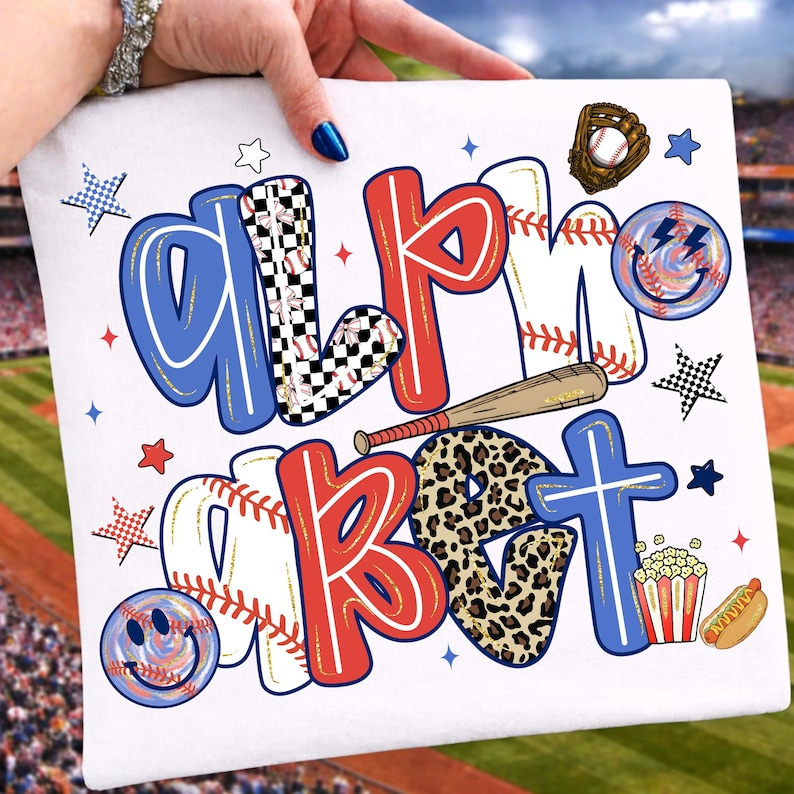 Op de afbeelding: Wit T-shirt met het woord "ALPHABET" in een honkbalthema. De letters zijn versierd met honkballen, luipaardprint en dambordpatronen. Een honkbalknuppel, handschoen en voedseliconen maken het ontwerp compleet.