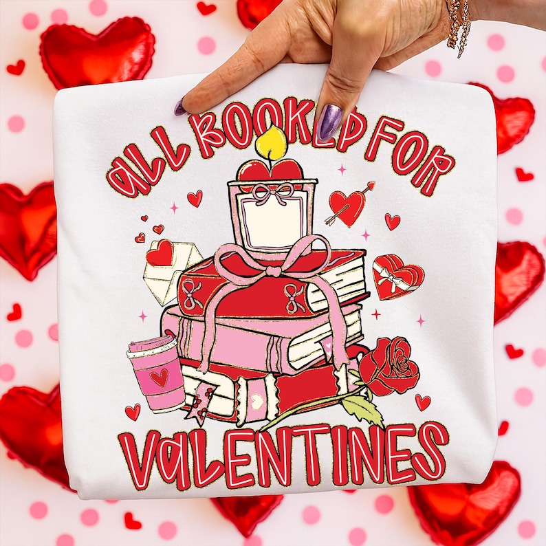 May include: White sweatshirt with a Valentine's Day graphic. The design features a stack of books, a candle, a coffee cup, and a rose. The text reads "ALL BOOKED UP FOR VALENTINES" in red.