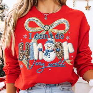 May include: Red sweatshirt with a festive design. Features a bow, snowflakes, and the text "I don't do winter very well." The word "winter" has a leopard print pattern. A snowman with a blue hat and scarf is in the design.