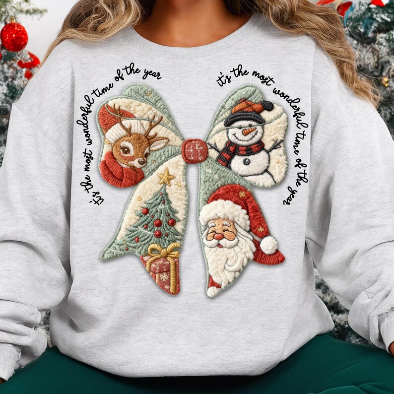 May include: A light gray sweatshirt featuring a large bow design with Christmas-themed elements. The bow includes a reindeer, snowman, Christmas tree, Santa Claus, and a wrapped gift. The text "It's the most wonderful time of the year" is written around the bow.