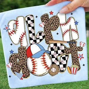 May include: Light blue baseball-themed graphic design on a light blue background. The design includes the words "Mom" and "Heart" with baseballs, a baseball cap, a bat, and stars. The letters have a mix of leopard print, baseball stitching, and checkered patterns.