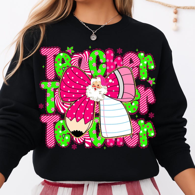 Peut inclure: Sweat-shirt noir avec un motif festif avec le mot "Teacher" en vert et rose, orn&eacute; de flocons de neige et d'un n&oelig;ud du P&egrave;re No&euml;l. Le n&oelig;ud est rose avec des pois blancs et un crayon.