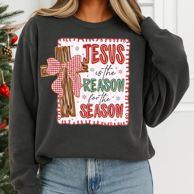 May include: Dark gray sweatshirt featuring a graphic with a cross and the text "JESUS is the REASON for the SEASON" in red, green, and white. The cross has a red and white plaid bow. A festive holiday-themed apparel item.