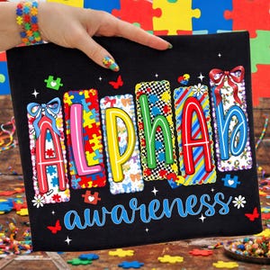 May include: Black canvas featuring the words "ALPHABET awareness" in vibrant colours. Each letter has a unique design, incorporating puzzle pieces, bows, and floral elements. Butterflies and hearts are scattered around the text.