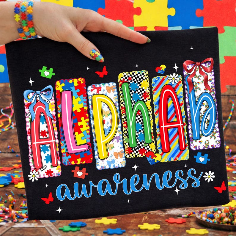 May include: Black canvas featuring the words "ALPHABET awareness" in vibrant colours. Each letter has a unique design, incorporating puzzle pieces, bows, and floral elements. Butterflies and hearts are scattered around the text.