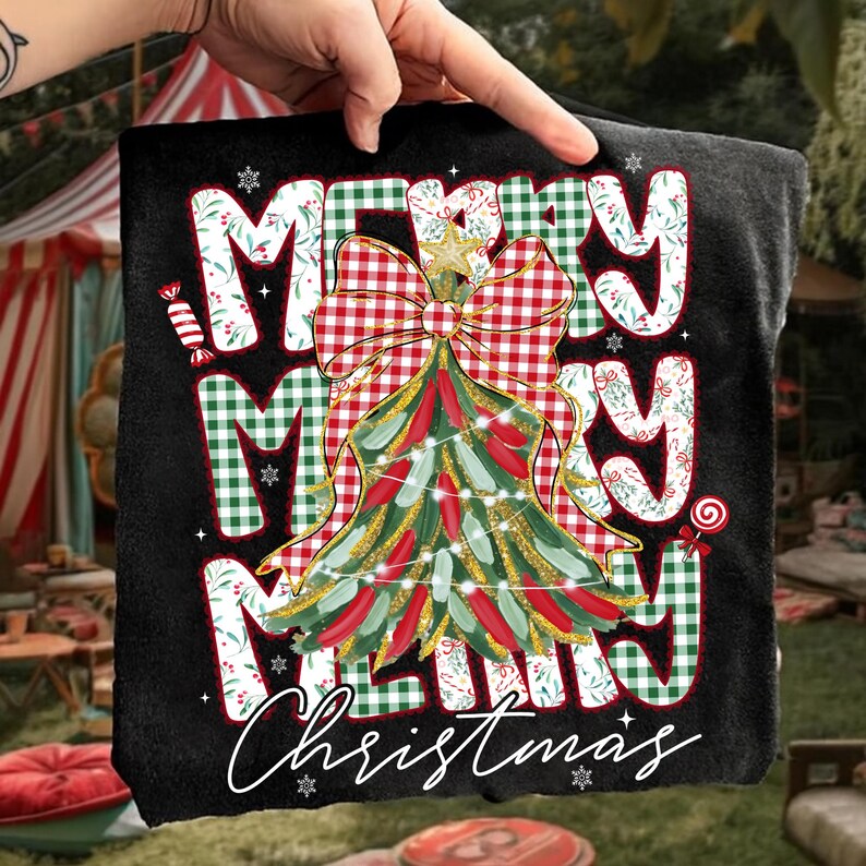 May include: Black t-shirt with a festive Christmas design. The design features the words "MERRY MERRY MERRY Christmas" in a mix of white, red, and green fonts. A Christmas tree with a red bow and gold accents is in the center.