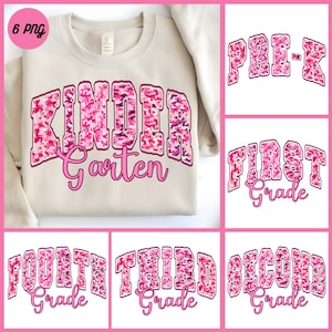 May include: A beige sweatshirt with the words "Kindergarten" in a pink camouflage design. Additional graphics include "Pre-K", "First Grade", "Fourth Grade", "Third Grade", and "Second Grade" in a similar style.