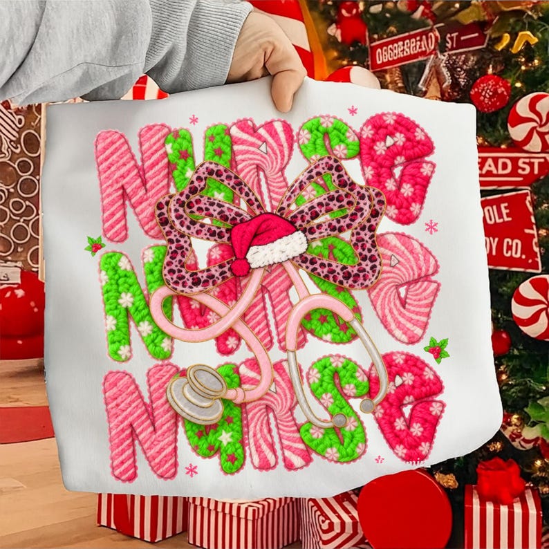 May include: A white tote bag featuring the word "NURSE" in pink and green candy cane-style letters. A pink stethoscope and a bow with a Santa hat are also featured. The bag is decorated with small stars and holly.