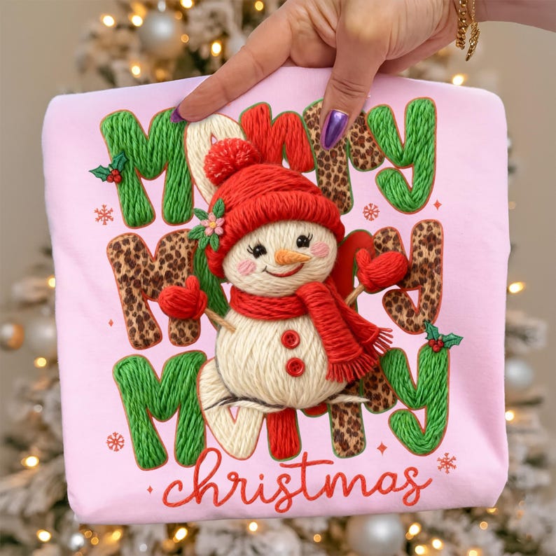 May include: Pink sweatshirt with the words "Merry Christmas" and a snowman design. The letters "M" and "Y" are green, and the letters "R" and "S" are leopard print. The snowman has a red hat, scarf, and mittens.