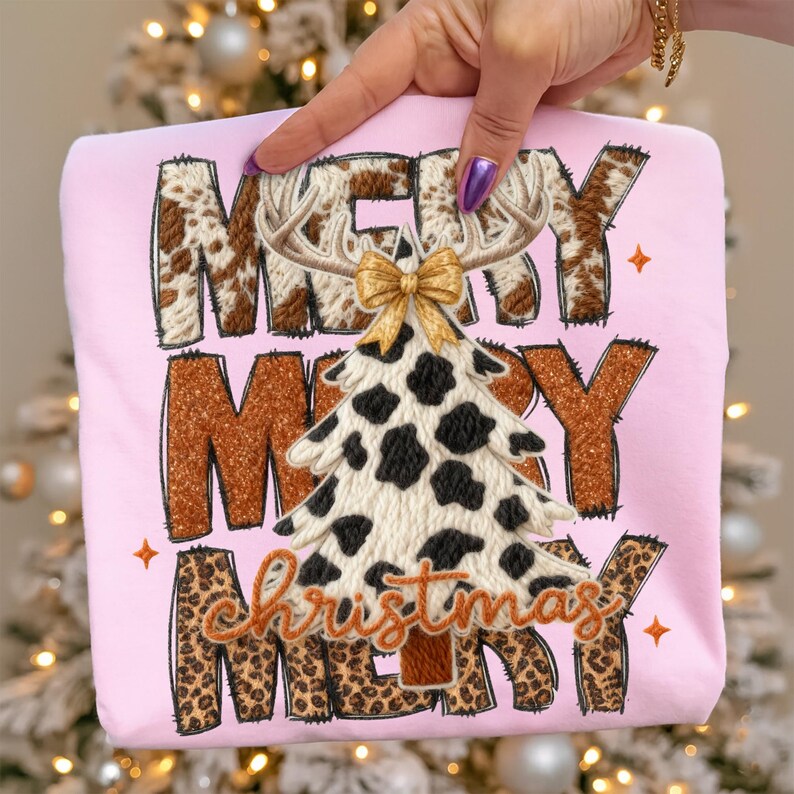 May include: A light pink sweatshirt with the words "MERRY CHRISTMAS" in a mix of brown cowhide, leopard print, and glittery brown lettering. A Christmas tree with cow spots and a gold bow is in the center.