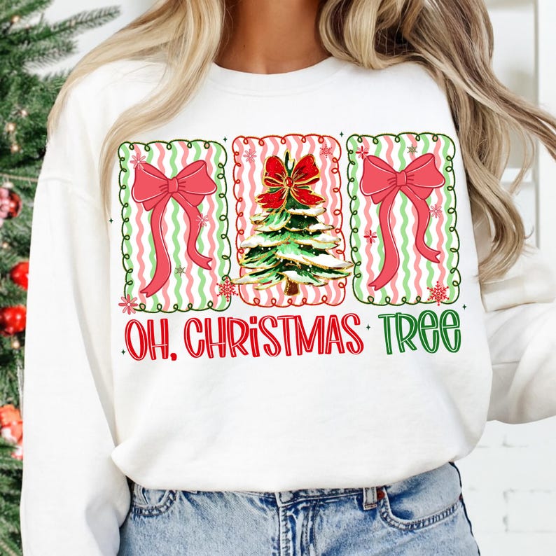 May include: White sweatshirt with a festive design featuring three framed images. The frames have a green and pink wavy pattern. The center image is a Christmas tree with a red bow, flanked by images of red bows. The text "OH. CHRISTMAS TREE" is below.