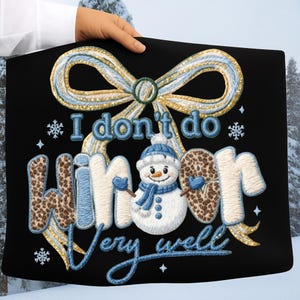 May include: Black tote bag with an embroidered design featuring a snowman, snowflakes, and the phrase "I don't do winter very well." The design includes a blue and gold bow and lettering.