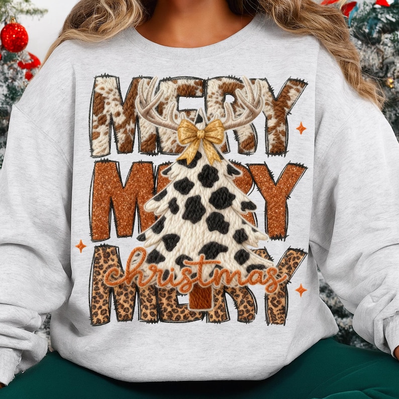May include: A light gray sweatshirt with a festive Christmas design. The design features the words "MERRY CHRISTMAS" in a mix of brown cow print and leopard print. A Christmas tree with a cow print pattern and antlers is in the center.