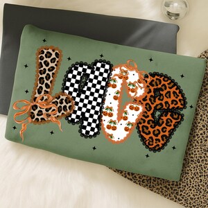 May include: Green decorative pillow with the word "LOVE" in a mix of patterns. The "L" is leopard print, the "O" is a black and white checkerboard, the "V" is decorated with pumpkins, and the "E" is leopard print. The pillow has a black lace trim.