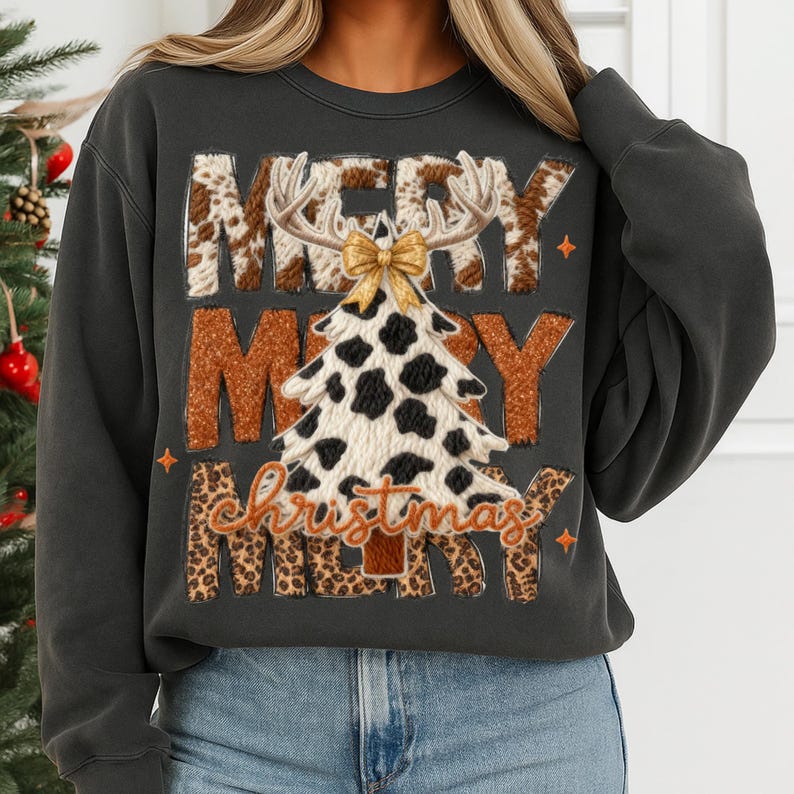 May include: Dark gray sweatshirt with a festive Christmas design. The design features the words "MERRY CHRISTMAS" with a cow print Christmas tree, antlers, and a gold bow. The sweatshirt is paired with blue jeans.