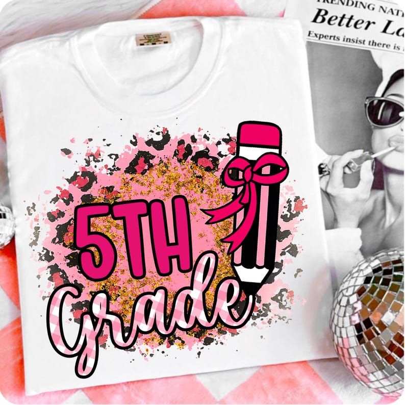 May include: White t-shirt featuring a pink and black leopard print design with gold glitter accents. The shirt has the words "5TH Grade" in pink and white, along with a pink bow-tied pencil graphic. A back-to-school theme.