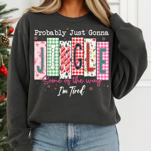 May include: Dark gray sweatshirt with the text "Probably Just Gonna Jingle Some of the way I'm Tired." The word "JINGLE" is in colorful, patterned blocks. Festive holiday apparel.