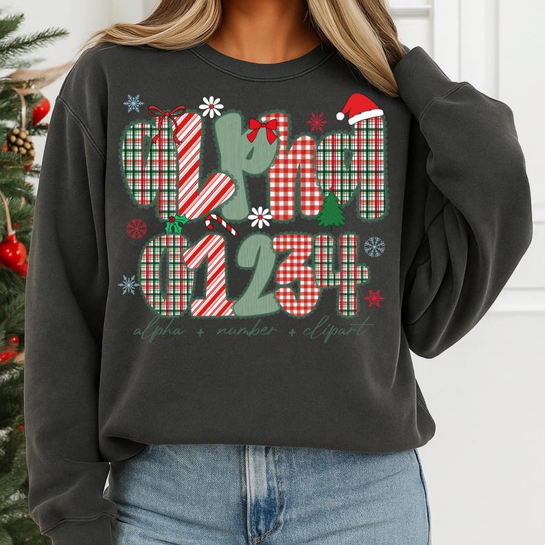 May include: Dark gray sweatshirt with a Christmas-themed design. The design includes the words "alpha + number + clipart" and the numbers "01234" in a red and green plaid pattern, along with snowflakes, a Santa hat, and a Christmas tree.