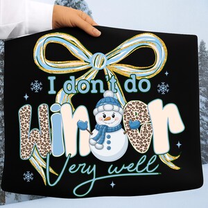 May include: Black tote bag featuring a snowman graphic and the phrase "I don't do winter very well." The design includes a blue and gold bow, snowflakes, and leopard print lettering. A fun winter-themed accessory.