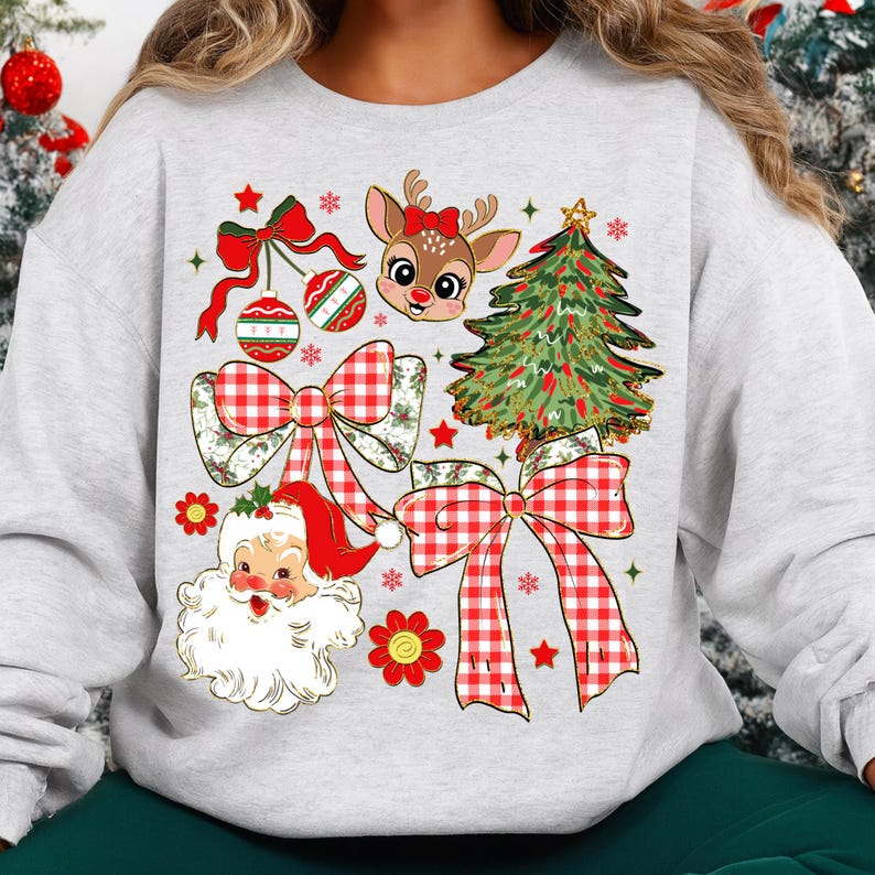 May include: A light grey sweatshirt with a festive Christmas design. The design includes a reindeer with a red bow, a Christmas tree, Santa Claus, red bows, and ornaments. The design is in red, green, and white.