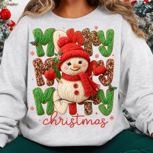 May include: A light gray sweatshirt with a festive Christmas design. The design features a snowman wearing a red hat, scarf, and mittens, with the words "Merry Christmas" in green and leopard print letters.