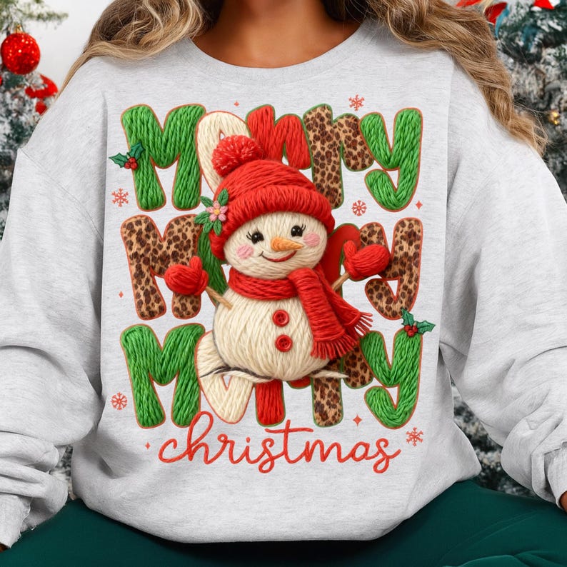 May include: A light gray sweatshirt with a festive Christmas design. The design features a snowman wearing a red hat, scarf, and mittens, with the words "Merry Christmas" in green and leopard print letters.