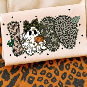May include: A light pink Halloween-themed graphic featuring the word "LOVE" with a ghost character holding a pumpkin. The letters have camouflage and leopard print patterns. The ghost is wearing a bow and giving a peace sign.