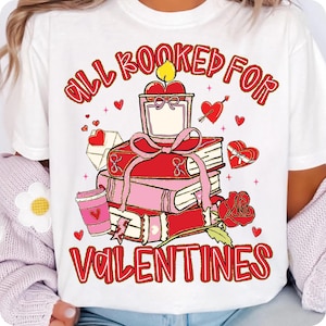 May include: White t-shirt with a Valentine's Day design. The graphic features a stack of books, a candle, a coffee cup, and a rose. The text reads "ALL BOOKED FOR VALENTINES" in red script.