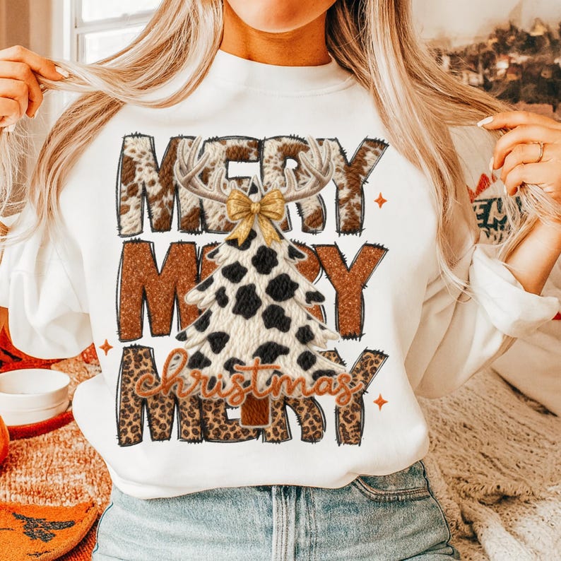 May include: White sweatshirt with a Christmas tree design. The tree is made of a cow print pattern with a gold bow and antlers. The words "Merry Christmas" are printed on the front in a mix of fonts and patterns.