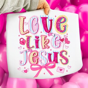 May include: A white print with the words "Love Like Jesus" in colorful, decorative lettering. The design includes hearts, a lock, a bow, and a rose, all in shades of pink, yellow, and blue.