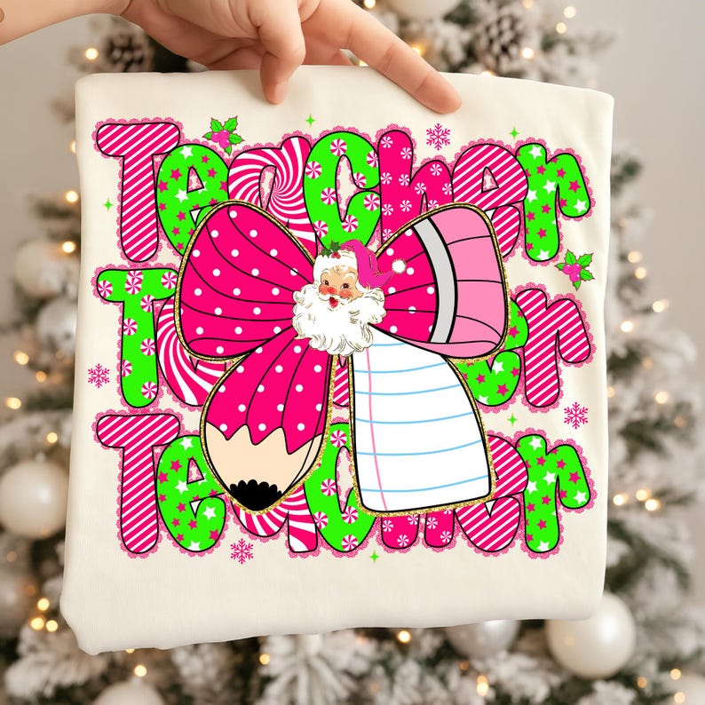Peut inclure: T-shirt cr&egrave;me avec un motif de No&euml;l. Le graphisme comprend le mot "Teacher" en rose et vert, un n&oelig;ud rose &agrave; pois, un crayon et une illustration du P&egrave;re No&euml;l. Des flocons de neige et des accents de houx compl&egrave;tent le th&egrave;me festif.