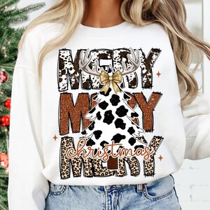 May include: White sweatshirt with a Christmas tree design. The tree is white with black spots, antlers, and a gold bow. The words "MERRY CHRISTMAS MERRY" are printed in brown and leopard print.