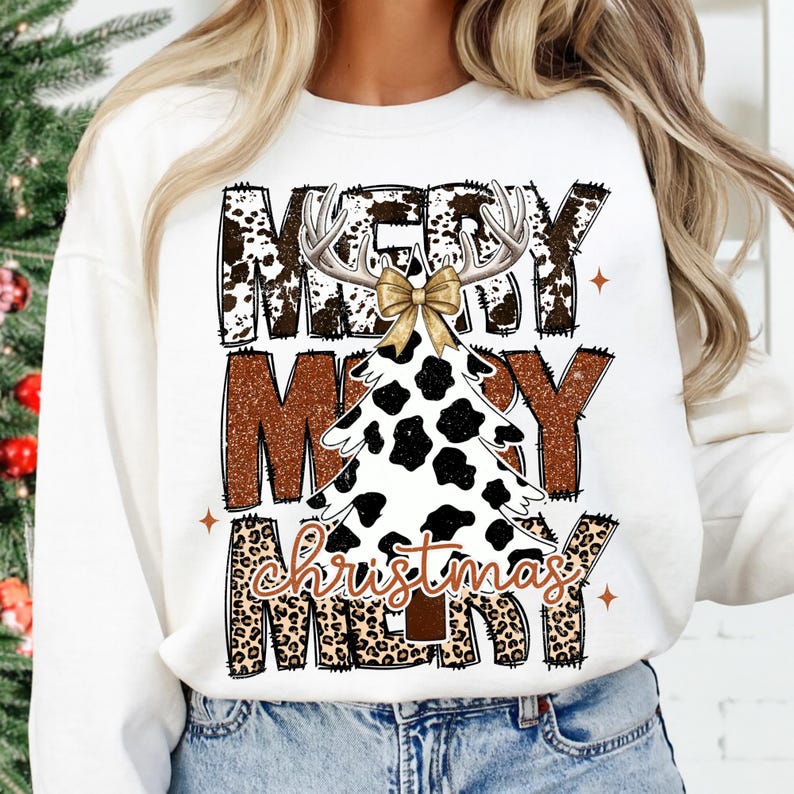 May include: White sweatshirt with a Christmas tree design. The tree is white with black spots, antlers, and a gold bow. The words "MERRY CHRISTMAS MERRY" are printed in brown and leopard print.
