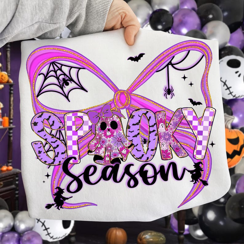 May include: White sweatshirt featuring a purple bow design and the words "Spooky Season". The design includes a ghost, bats, spiders, and a spiderweb, ideal for Halloween celebrations.