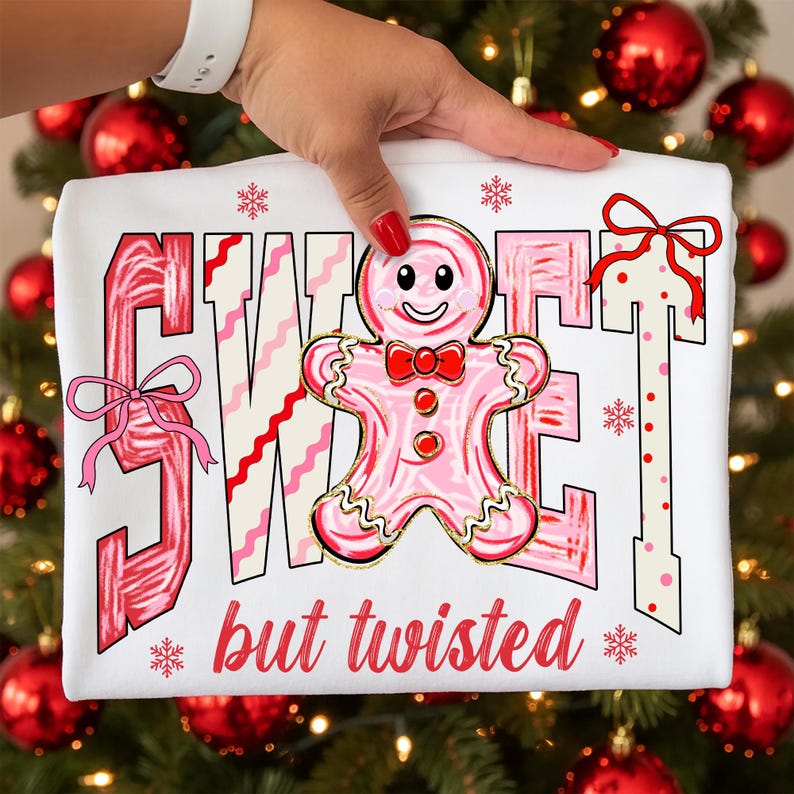 May include: White t-shirt featuring the words "SWEET" and "but twisted" in pink and red. A pink gingerbread man with a red bow tie is in the center. The design has a festive, Christmas theme.