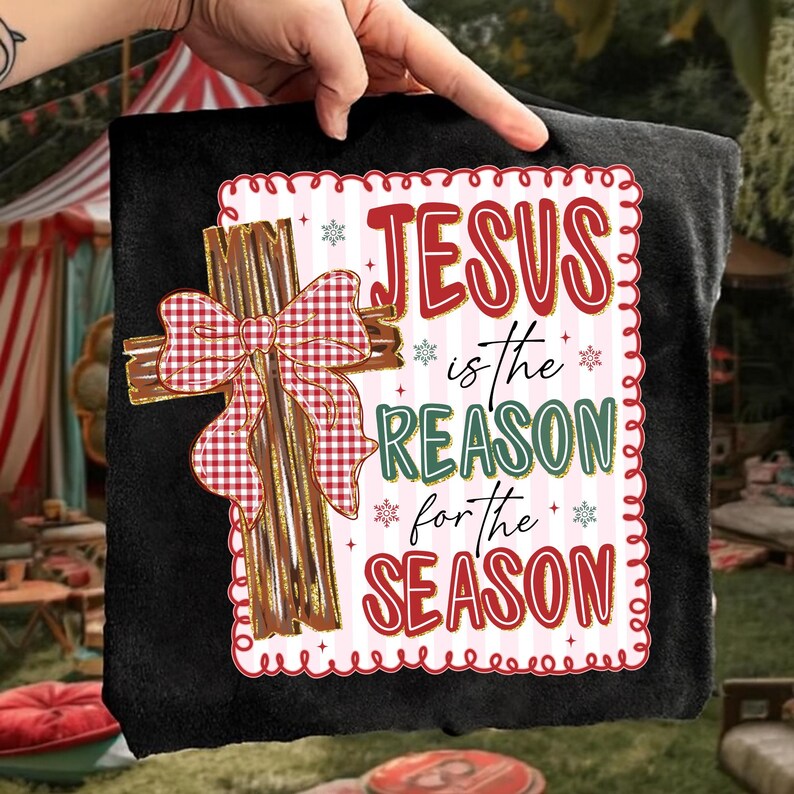 May include: Black t-shirt featuring a decorative cross with a red and white gingham bow. The text "JESUS is the REASON for the SEASON" is displayed in red and green, with snowflake accents, within a decorative border.