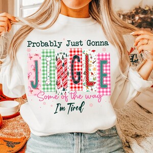 May include: White sweatshirt with the text "Probably Just Gonna JINGLE Some of the way I'm Tired." The word "JINGLE" is in colorful, festive blocks with holiday-themed patterns and designs, perfect for Christmas.