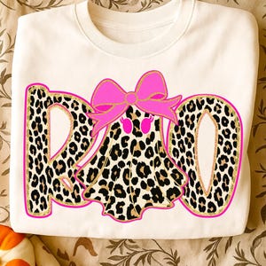 May include: White sweatshirt with a leopard print "BOO" design. The letters are outlined in gold glitter and pink. A leopard print ghost with a pink bow is in the center of the "O".