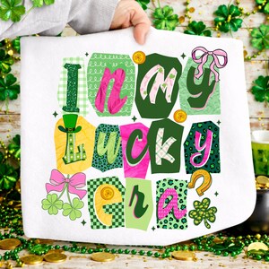 May include: White St. Patrick's Day themed towel with the phrase "I'm my lucky era" in colorful, patterned letters. The design includes shamrocks, a horseshoe, and a leprechaun hat. The towel is held up by a person.