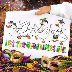 May include: A white sign with three cartoon geese wearing jester hats and beaded necklaces. The geese are dancing, and one is playing a drum. The sign reads "Let the Good Times Roll" in colorful letters. Mardi Gras masks and beads are in the foreground.