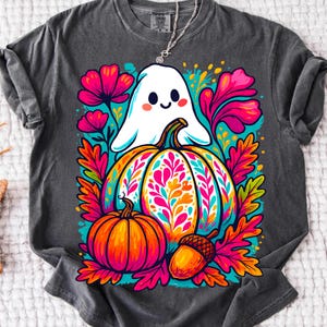 May include: Dark gray t-shirt featuring a colorful Halloween design. A smiling white ghost hovers above a large pumpkin with a floral pattern. A smaller pumpkin and an acorn are also present, surrounded by pink, orange, and teal foliage.