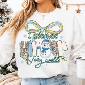 May include: White sweatshirt with a winter-themed graphic. The design includes a snowman wearing a blue hat and scarf, and the text "I don't do winter very well." The word "winter" has a leopard print pattern.