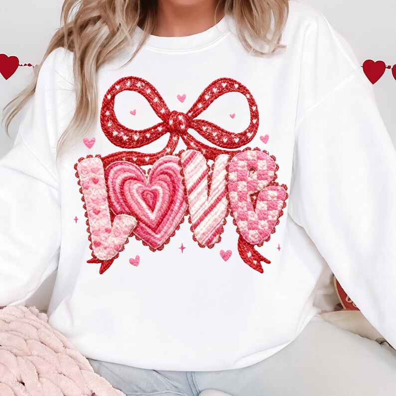 May include: White sweatshirt with a red bow and the word "LOVE" in pink and red, featuring a heart-shaped "O". The design includes small hearts and stars, perfect for Valentine's Day or expressing affection.