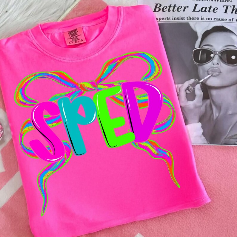 May include: Bright pink t-shirt with the word "SPED" in large, colorful letters. The letters are outlined in black and have a 3D effect. A large, multi-colored bow design is above the letters. The shirt has a tag that says "Comfort Colors".