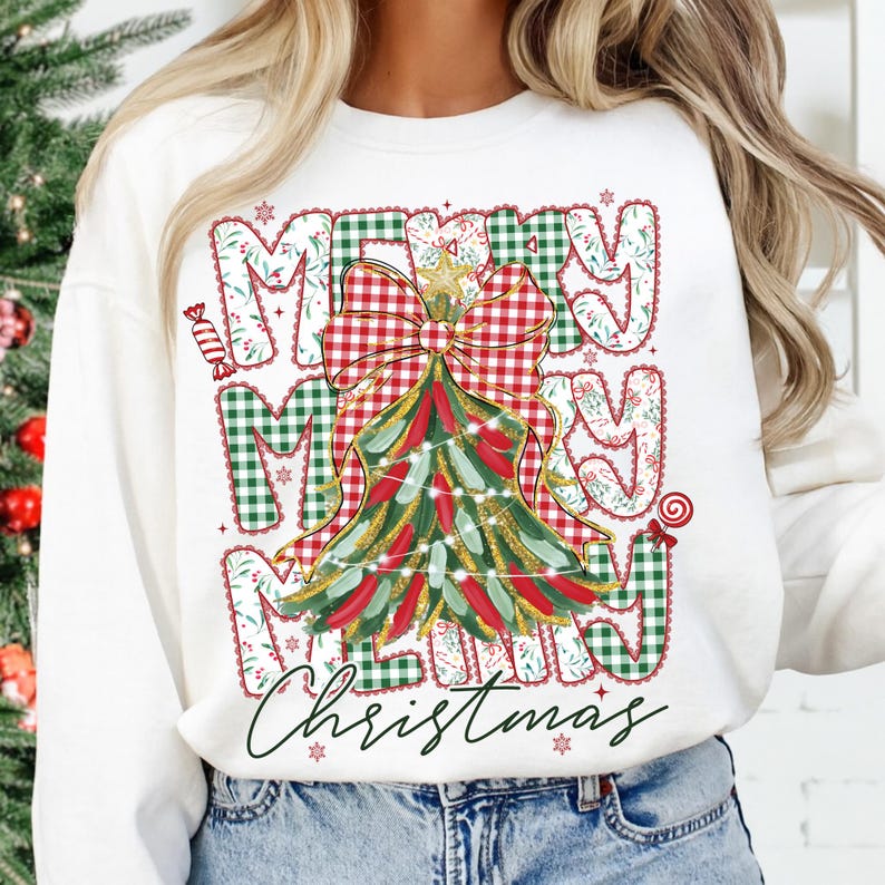 May include: White sweatshirt with a festive Christmas design. The design features the words "MERRY CHRISTMAS" in a mix of green and red plaid and floral patterns, with a Christmas tree and bow.